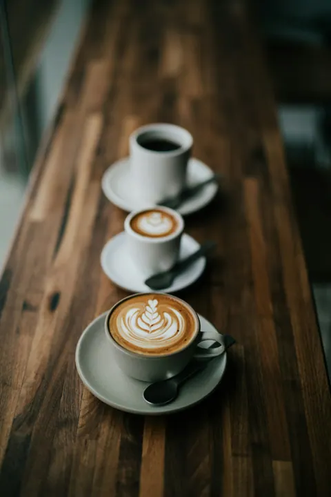 Three coffees waiting on a wooden café table.